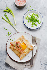 Crepe with fried egg, cheese, bacon and green onions for breakfast on a light gray concrete background.