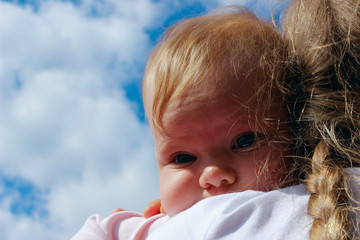 People, childhood, family concept. Cropped shot of a cute baby girl over blue sky background. Sisters hugs, close up. 