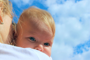 People, childhood, family concept. Cropped shot of a cute baby girl over blue sky background. Sisters hugs, close up. 