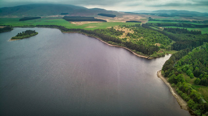 A blue loch with islands on green Scotish landscape