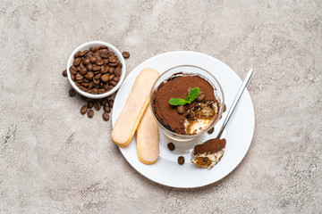 Portion of Classic tiramisu dessert in a glass, savoiardi cookies and cup of coffee on concrete background