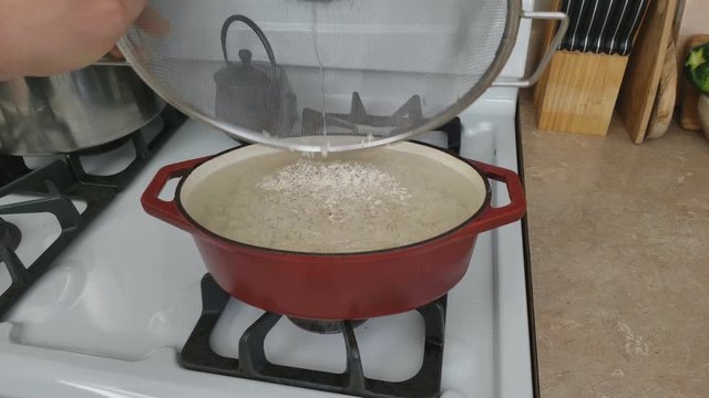 Home cooking - Adding previously washed and drained long grain rice to a heavy small oval enameled pot with some water already in ready to be slow cooked.