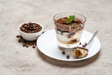 Portion of Classic tiramisu dessert in a glass cup on concrete background