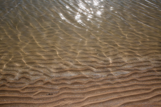 Sunlit Clear Water Over Wavy Sand Patterns