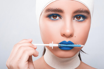 Beauty concept. Young model with blue lips and soft skin doing plastic surgery. Female with bandage on head, on light background. Girl want to do beautician injections with syringe.