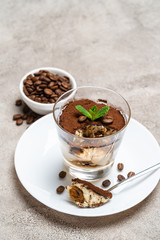 Portion of Classic tiramisu dessert in a glass cup on concrete background