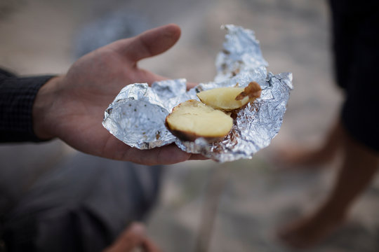 Hand holding baked potato pieces wrapped in aluminum foil outdoors