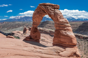 Close up of the iconic Delicate Arch in the Arches National Park, under a blue sky with puffy clouds