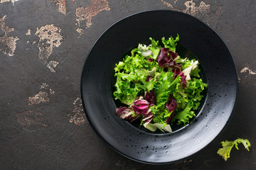 Mix fresh leaves of arugula, lettuce, spinach, beets for salad on a dark stone background. Selective focus.