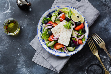 Traditional Greek Salad. Vegetarian dish with fresh lettuce, olives, peppers, cucumbers, onions and feta cheese. On dark rustic concrete background. Top view.