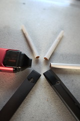 3 vape electronic cigarette devices and 3 cigarettes in a star pattern on a white textured background close up