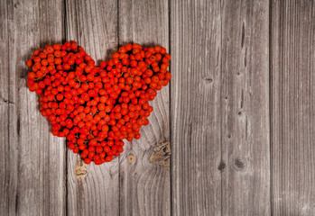 Autumn romantic composition. The heart is made of orange Rowan berries on a wooden background.