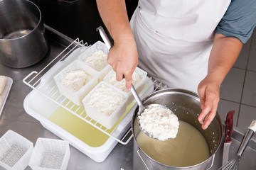 Cheesemaker pours the curdled milk into the plastic forms