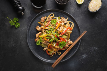 Udon stir-fry noodles with pork bowl and vegetables on black stone background. Asian cuisine.