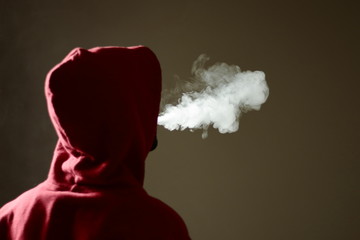 Young male in red hoodie vaping smoking, exhales thick vapor, isolated rear view