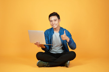 Happy excited Asian man holding laptop and raising his arm up to celebrate success or achievement.