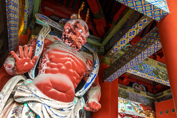 Close up of a huge wooden red statue portraying a jizo protector deity guarding the entrance of a...