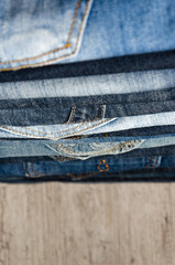 A stack of neatly folded jeans on wooden background. Close-up of jeans in different colors. Jeans texture or denim background. Copy space. Selective focus