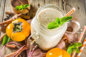 Autumn healthy drinks and snacks. Autumn seasonal persimmon smoothie with spices - cinnamon, anise, with mint leaves. On a rustic wooden background,
