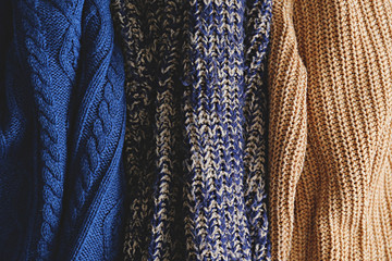 Bunch of knitted warm pastel color sweaters with different vertical knitting patterns hanging in bunch, clearly visible texture. Stylish fall / winter season knitwear clothing. Close up, copy space.