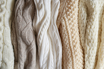 Bunch of knitted warm pastel color sweaters with different vertical knitting patterns hanging in...