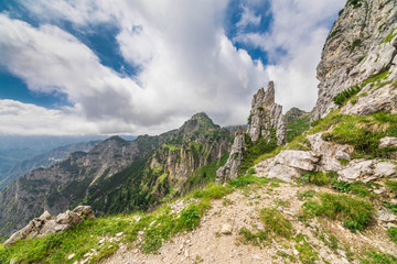 Italian alpine landscape, with dolomite-rock peaks surrounded by slopes covered in green grass, under a blue sky with puffy clouds