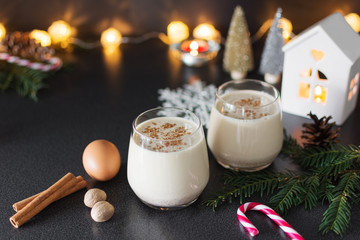 Fresh eggnog with cinnamon and nutmeg for christmas holiday with christmas decorations on dark background, low key.