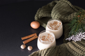 Fresh eggnog with cinnamon and nutmeg for christmas holiday with christmas decorations on dark background, low key.