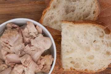 Canned cod liver in a bowl with two pieces of bread on a wooden board
