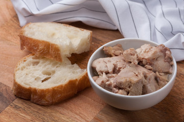 Canned cod liver in a bowl and two pieces of ciaabatta on a wooden board