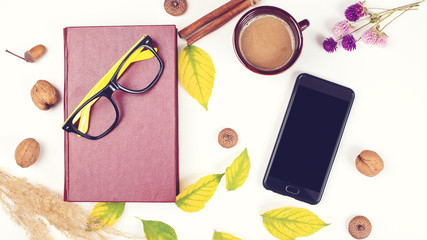 Autumn background with cup of coffee, book, mobile phone and autumn leaves. Mockup with smartphone and autumn decoration. Autumn time for reading