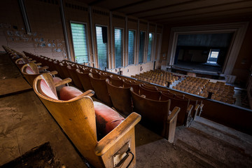 Wide angle shot of the interior of an old and abandoned cinema, with the back rows in foreground and the screen in the background