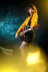 Fototapeta premium Portret pięknej młodej kobiety hipster z kręconymi włosami z czerwoną gitarą w neony. Muzyk rockowy gra na gitarze elektrycznej. Koncepcja stylu lat 90.