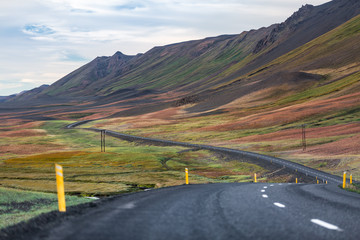 Icelandic landscape with a road snaking through a colorful sloping crested hill and a plain