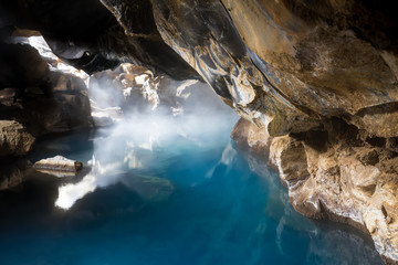 Icelandic natural cave flooded with steaming blue geothermal water