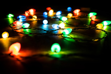 Christmas tree branch and lights on wooden background. View with copy space. Colored lights on a Christmas garland in the dark of night