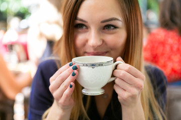 Cute girl sipping coffee out of a vintage tea cup in cafe