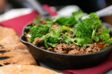 Shakshuka with sausage, tomatoes, egg, parsley, in cast iron skillet with pita bread