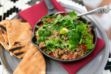 Shakshuka with sausage, tomatoes, egg, parsley, in cast iron skillet with pita bread