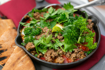 Shakshuka with sausage, tomatoes, egg, parsley, in cast iron skillet with pita bread