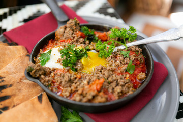 Shakshuka with sausage, tomatoes, egg, parsley, in cast iron skillet with pita bread