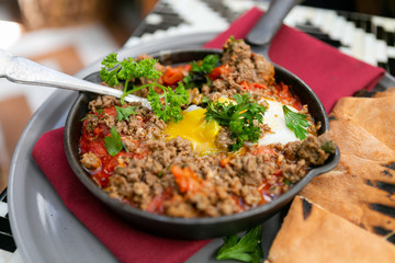 Shakshuka with sausage, tomatoes, egg, parsley, in cast iron skillet with pita bread