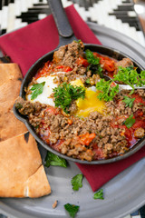 Shakshuka with sausage, tomatoes, egg, parsley, in cast iron skillet with pita bread