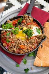Shakshuka with sausage, tomatoes, egg, parsley, in cast iron skillet with pita bread