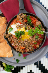Shakshuka with sausage, tomatoes, egg, parsley, in cast iron skillet with pita bread