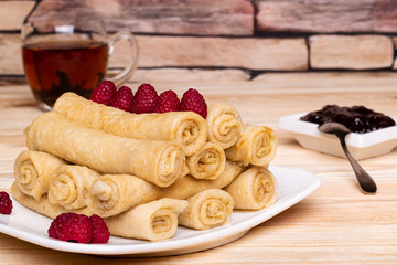 Fototapeta na wymiar A stack of crepes decorated with raspberries. A mug of black tea, a jam. Кussian pancakes with filling.