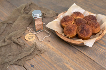 Homemade Muffins topped with Cinnamon Sugar in Rustic Setting; Wooden Bowl, Wooden Table, Cinnamon Sugar Jar in Background