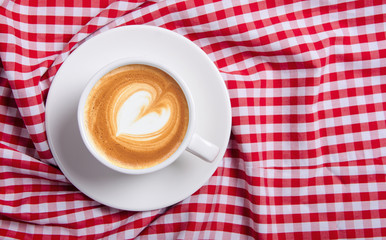 Cup of coffee on red kitchen tablecloth, relaxed morning atmosphere.