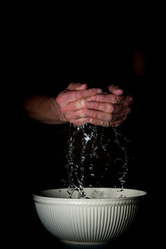 man washing his hands with water in white bowl. Dark background