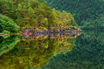 Fototapeta na wymiar Reflections in the calm water of the Norwegian crystal clear lake with a rocky bottom in a small town Skodje, Norway.